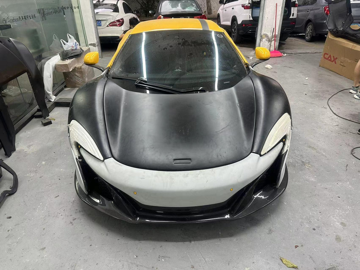 Front view of a McLaren supercar in a garage with a matte black hood and yellow accents