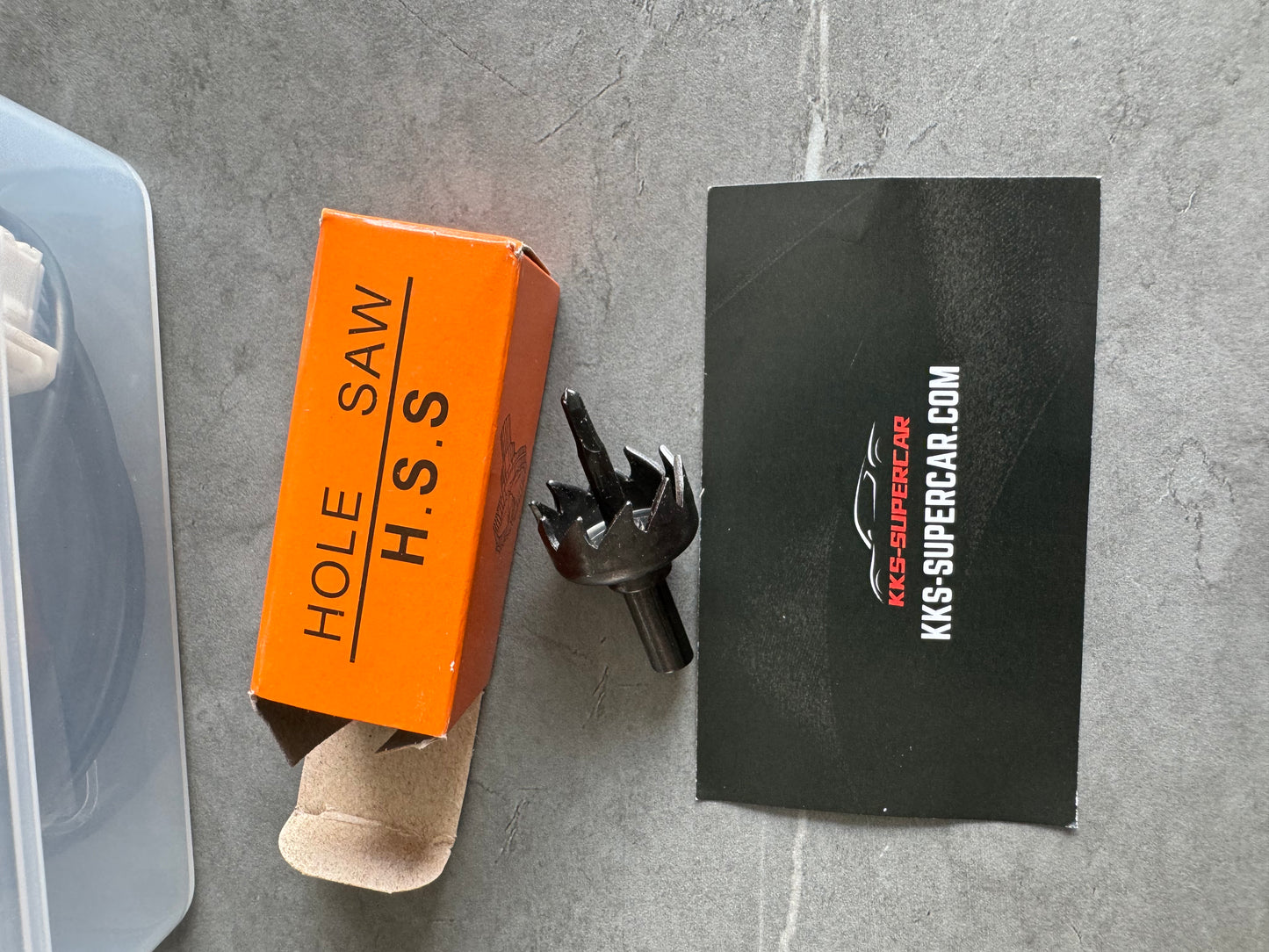HSS hole saw drill bit with box and business card on gray surface