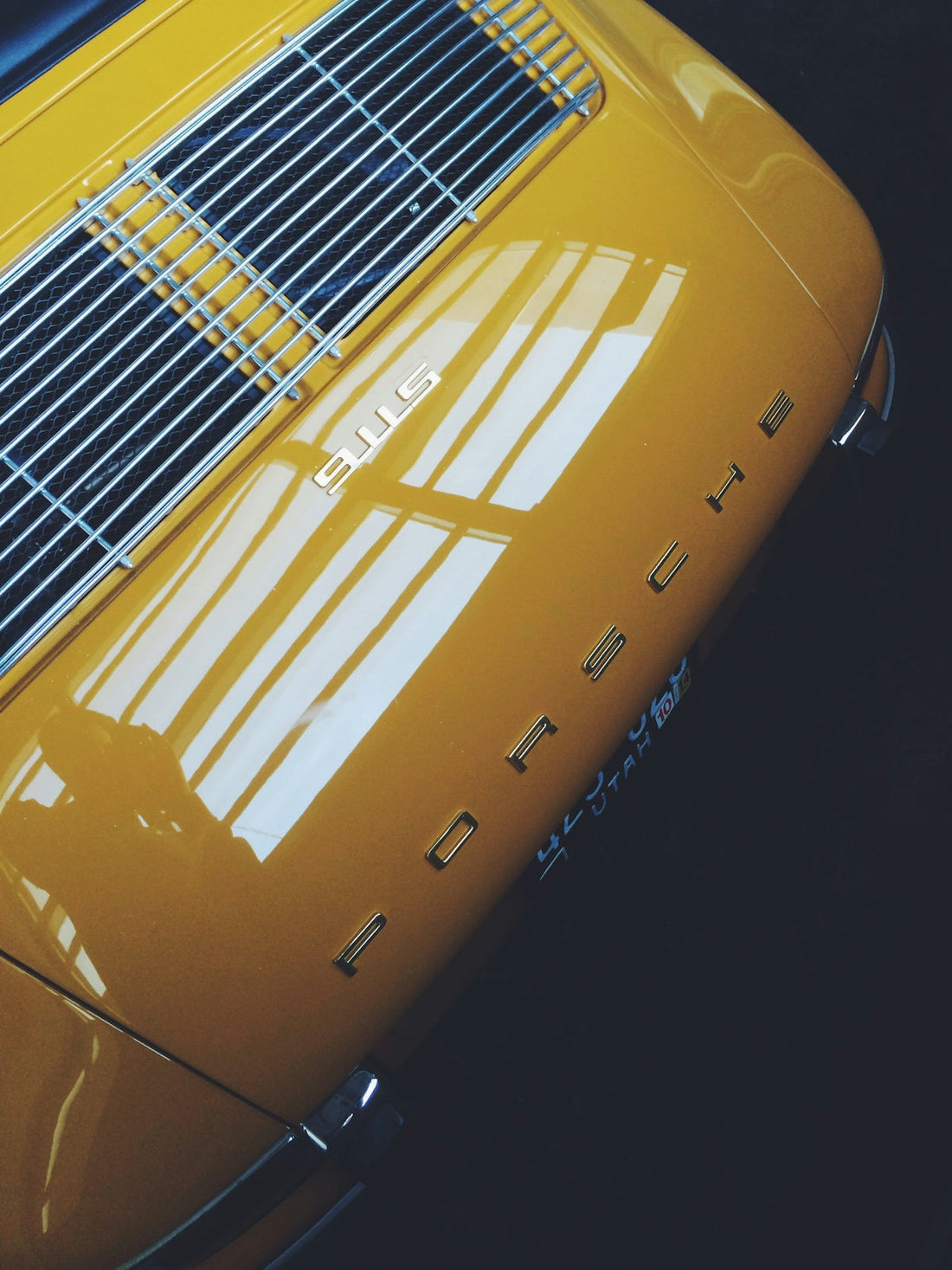 Yellow Porsche 911S rear deck with chrome grille and rear logo, luxury sports car closeup