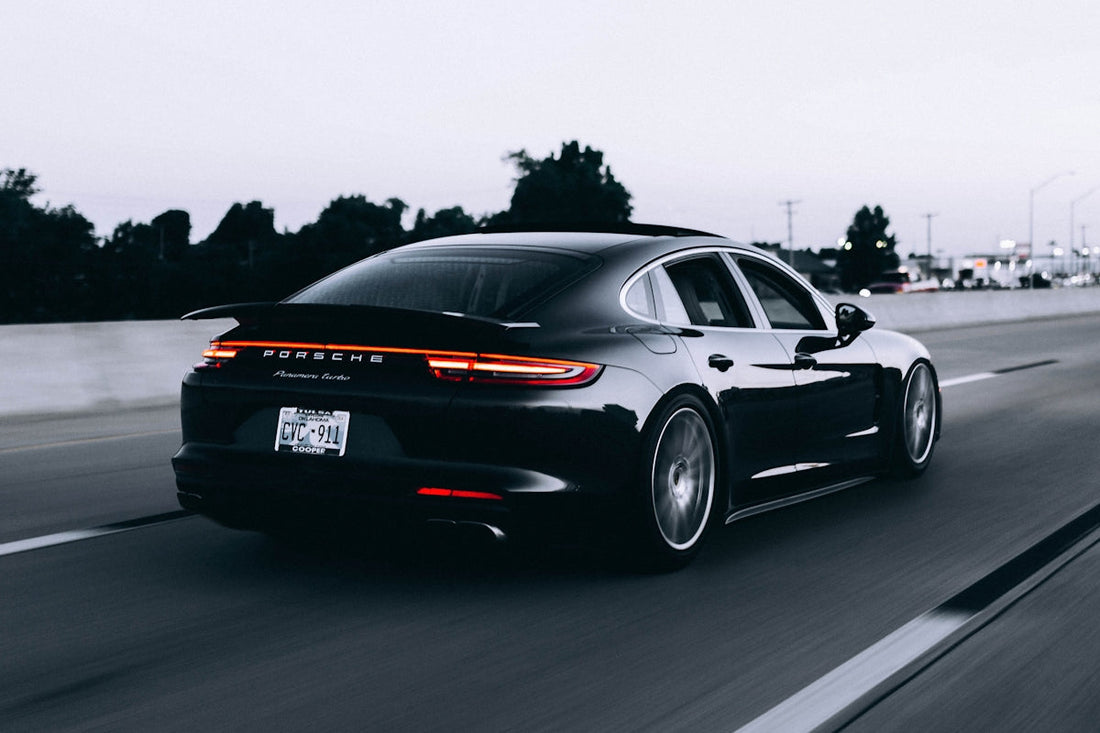 Black Porsche Panamera Turbo driving on highway at dusk, LED tail lights glowing