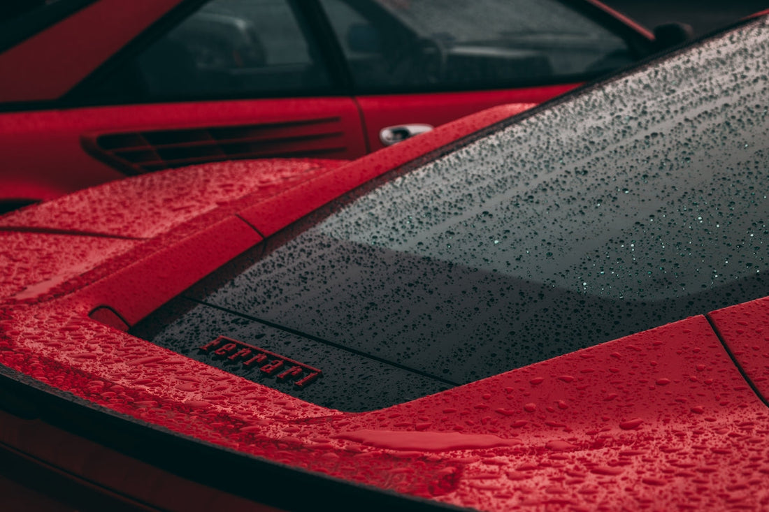 Close-up of red Ferrari supercar rear in rain, water drops on window and bodywork