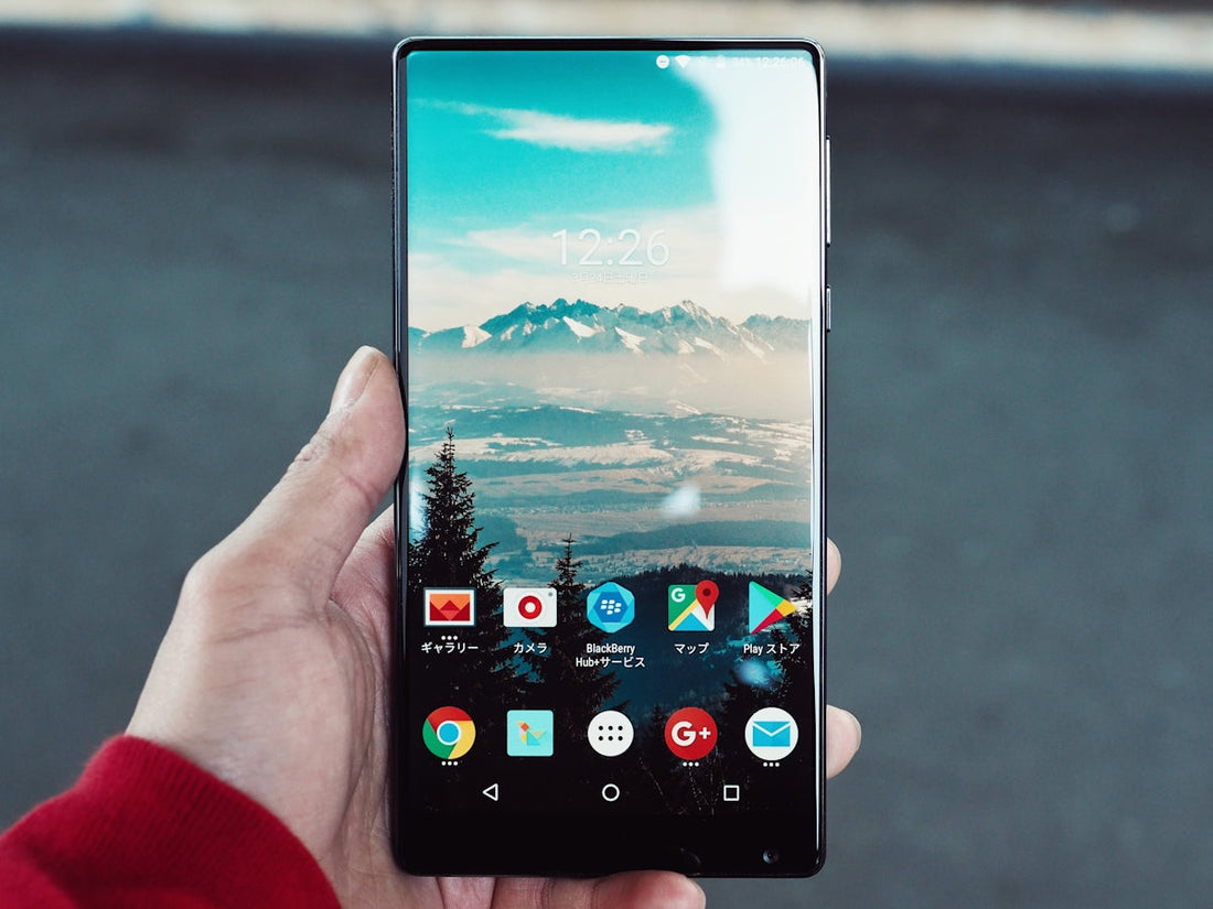 Hand holding a smartphone with a mountain landscape wallpaper and app icons visible.