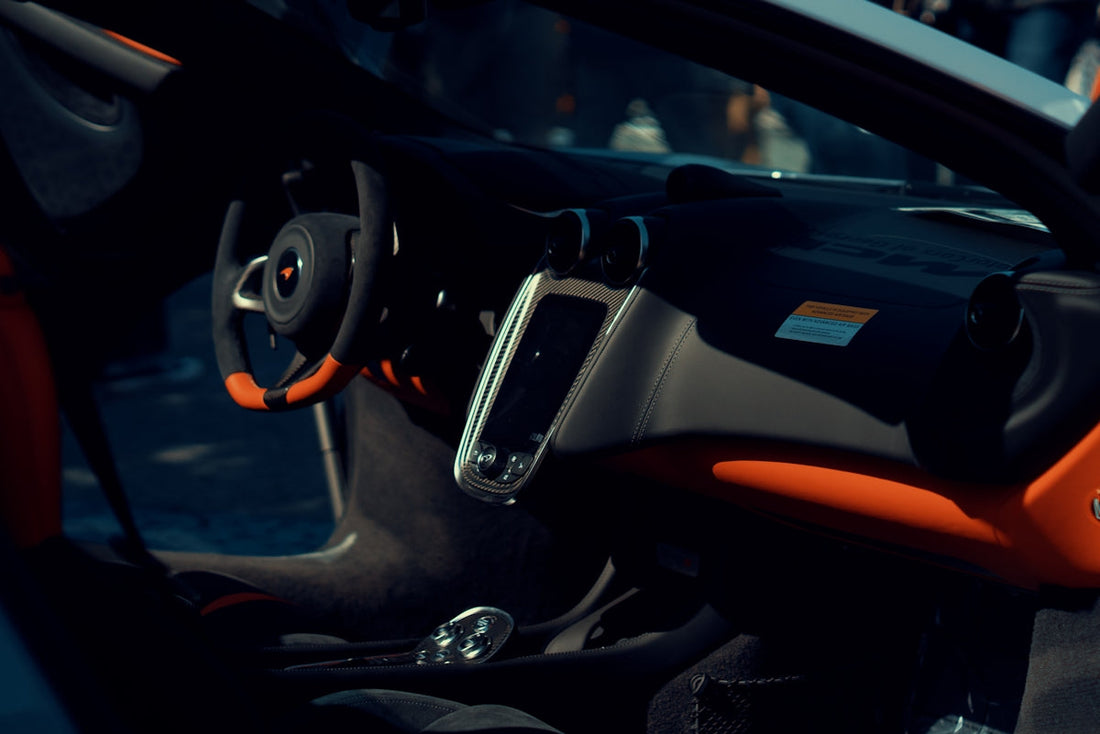 McLaren supercar interior with steering wheel, touchscreen, and orange accents
