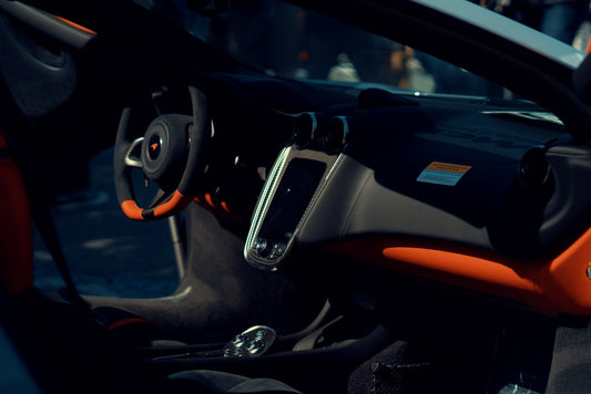 McLaren supercar interior with steering wheel, touchscreen, and orange accents