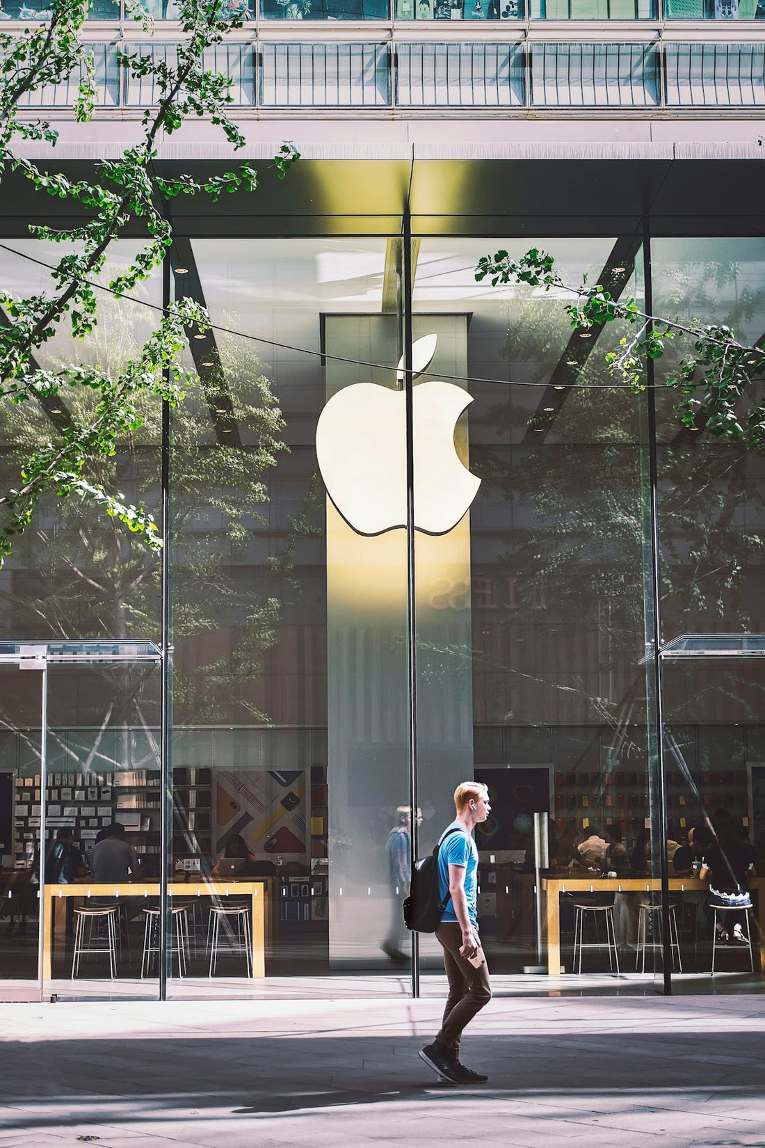 Person walking past Apple Store with large Apple logo on glass facade, urban setting