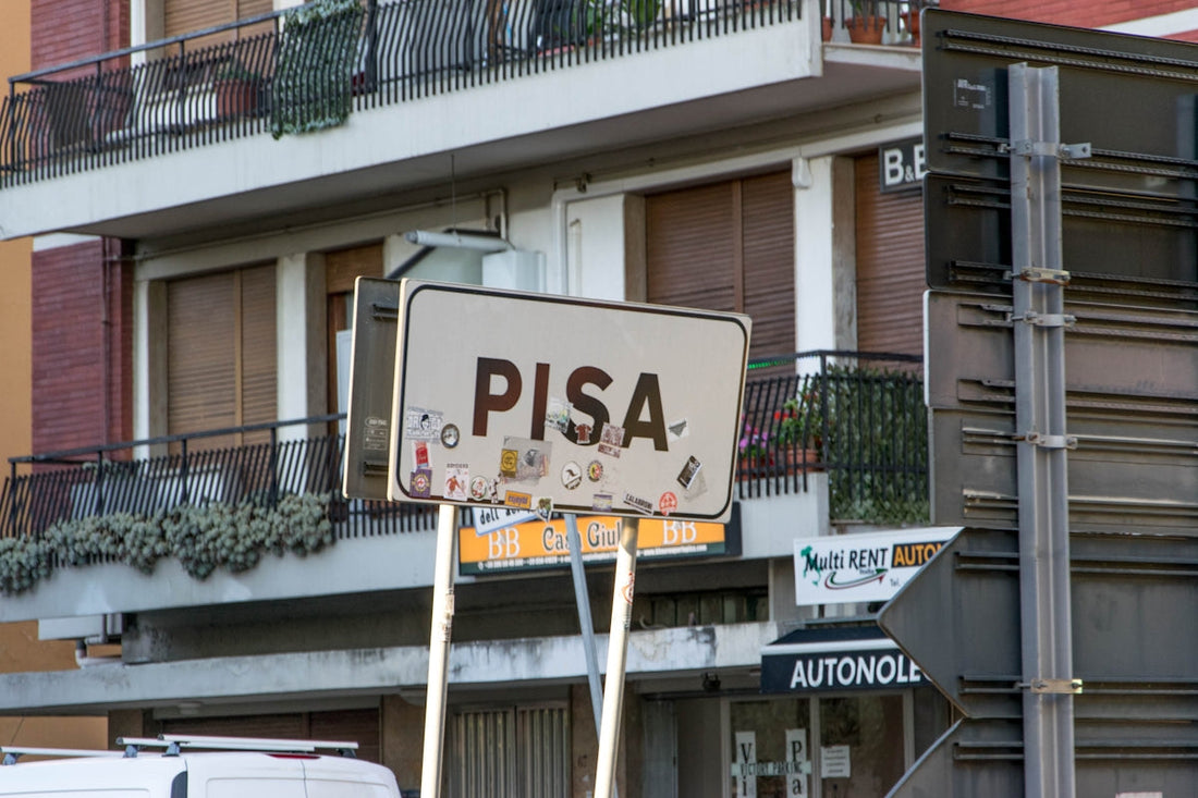 Pisa city road sign with stickers in front of urban apartment buildings