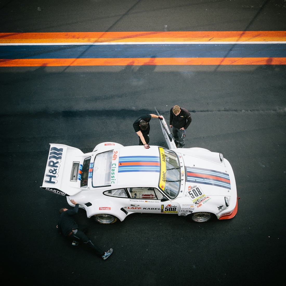 Vintage white race car with blue and red stripes on track, crew members inspecting vehicle
