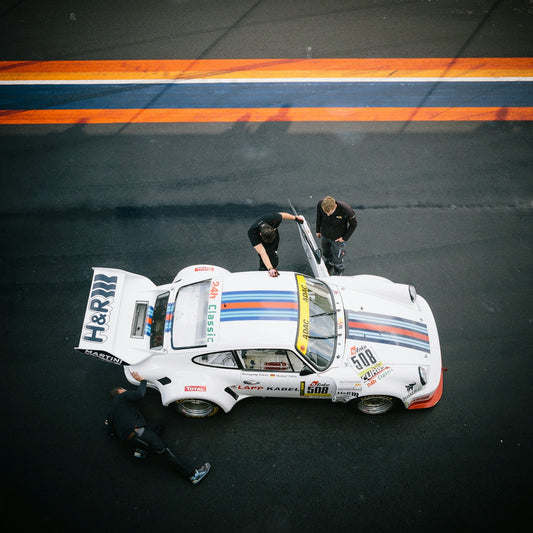 Vintage white race car with blue and red stripes on track, crew members inspecting vehicle