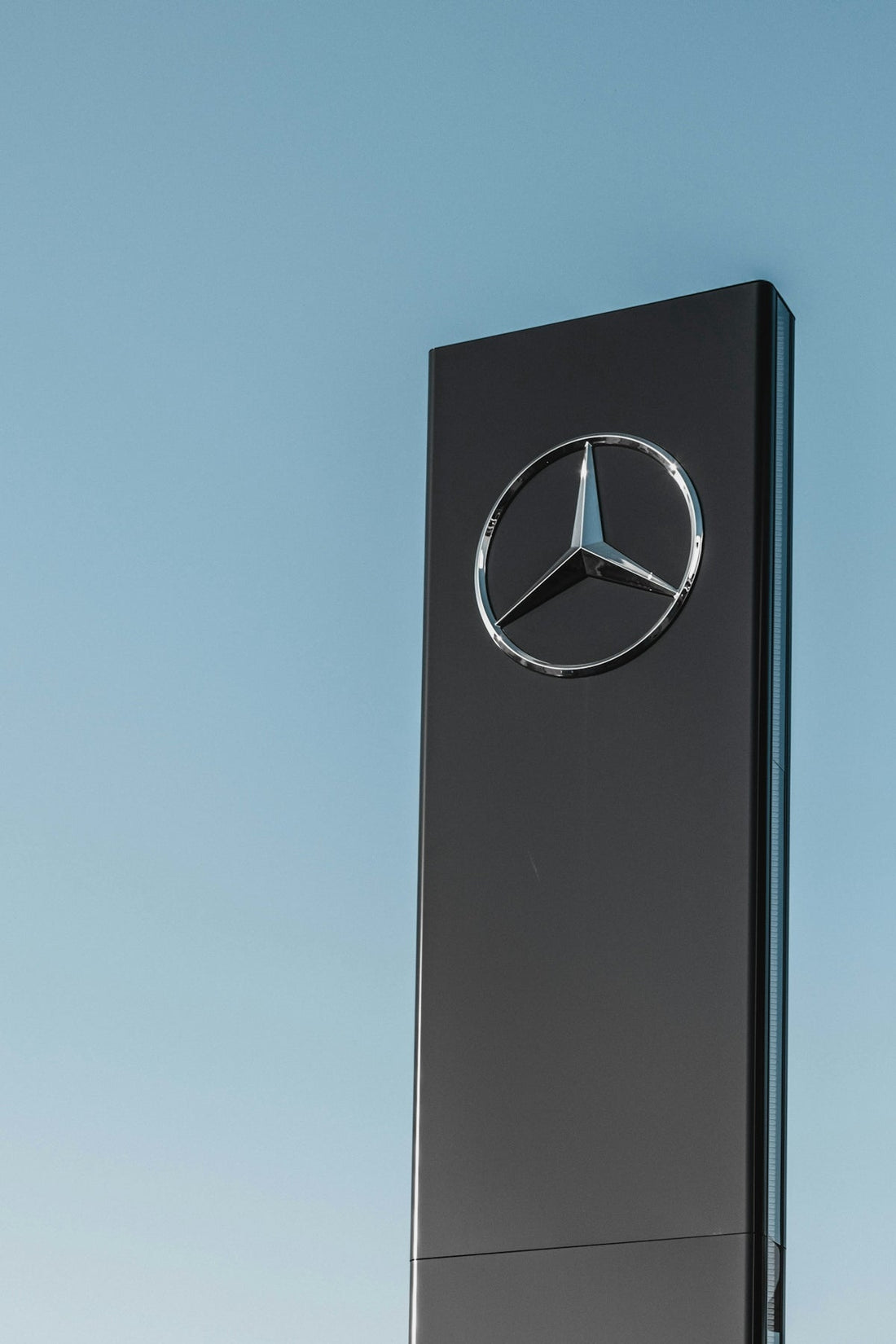 Luxury car dealership sign with chrome emblem against clear blue sky