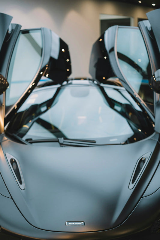 Matte grey McLaren supercar with butterfly doors open, showcased indoors