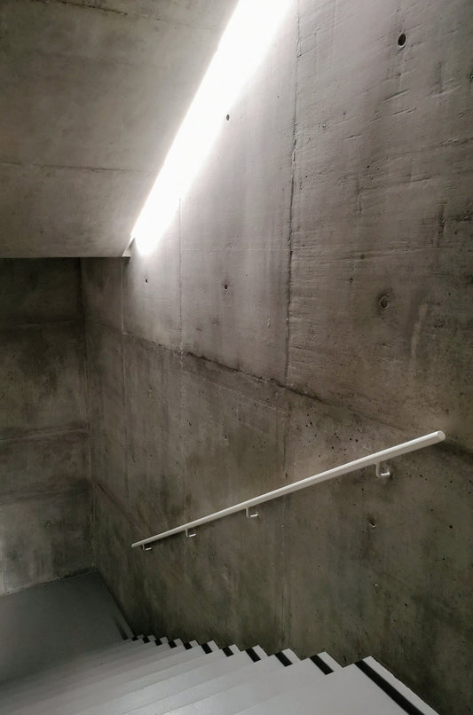 Modern concrete staircase with minimalist white handrail and linear ceiling light