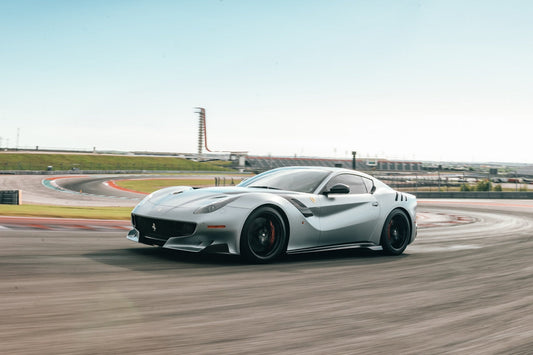 Silver Ferrari supercar driving on a racetrack with modern grandstands in background