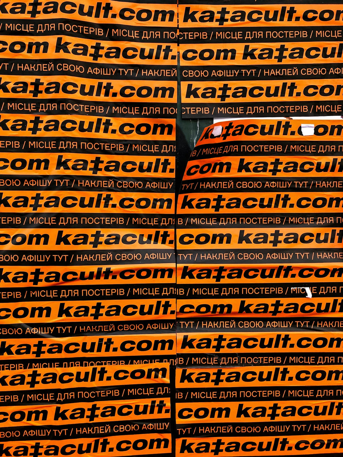 Bright orange posters with bold black text covering a sports car, exotic car hidden behind ads
