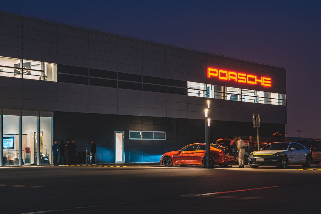Luxury sports cars parked at Porsche dealership at night, illuminated by red Porsche sign