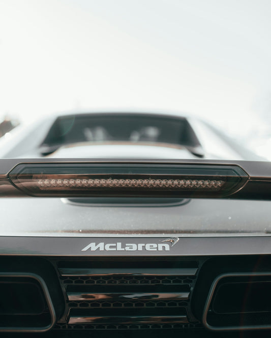 Close-up of McLaren supercar rear emblem, taillight, and vent under bright sky