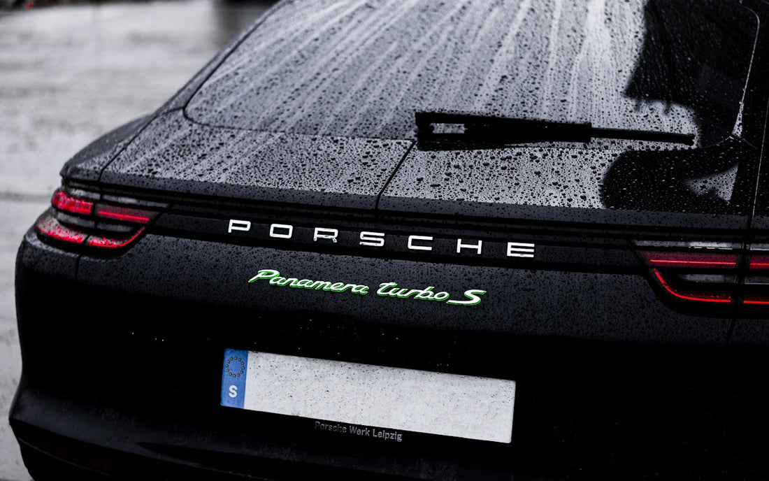 Rear view of a black Porsche Panamera Turbo S with rain droplets on the trunk and tail lights illuminated