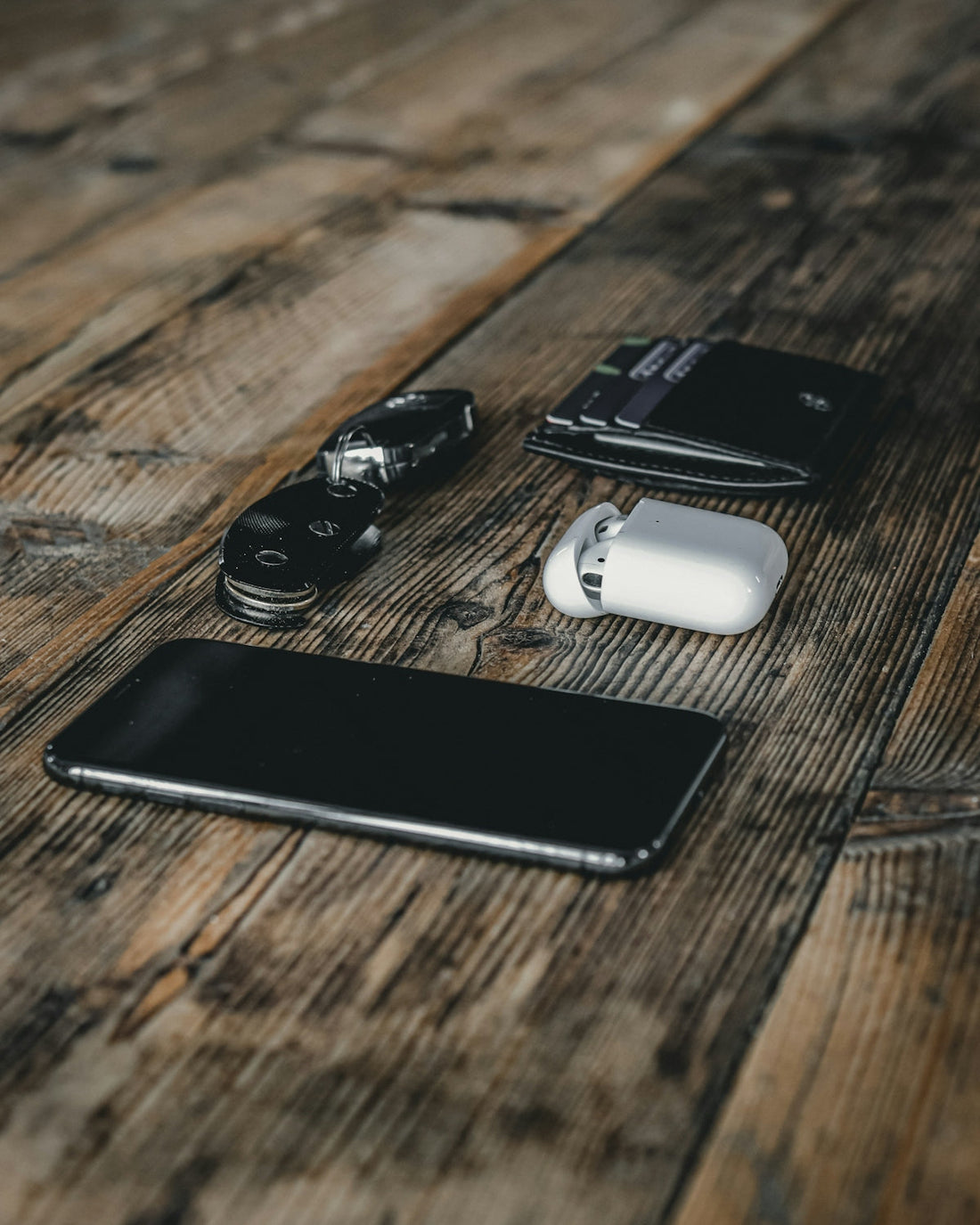 Luxury car key fob, smartphone, wallet, and AirPods on rustic wooden table