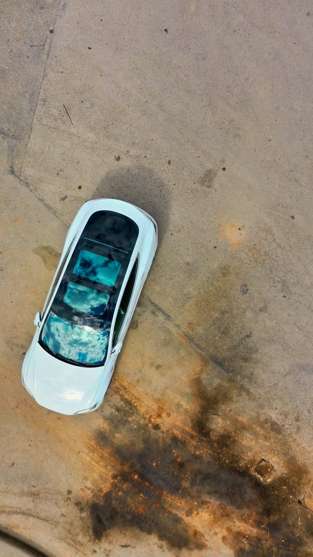 White luxury sports car with panoramic sunroof on concrete surface, top-down view