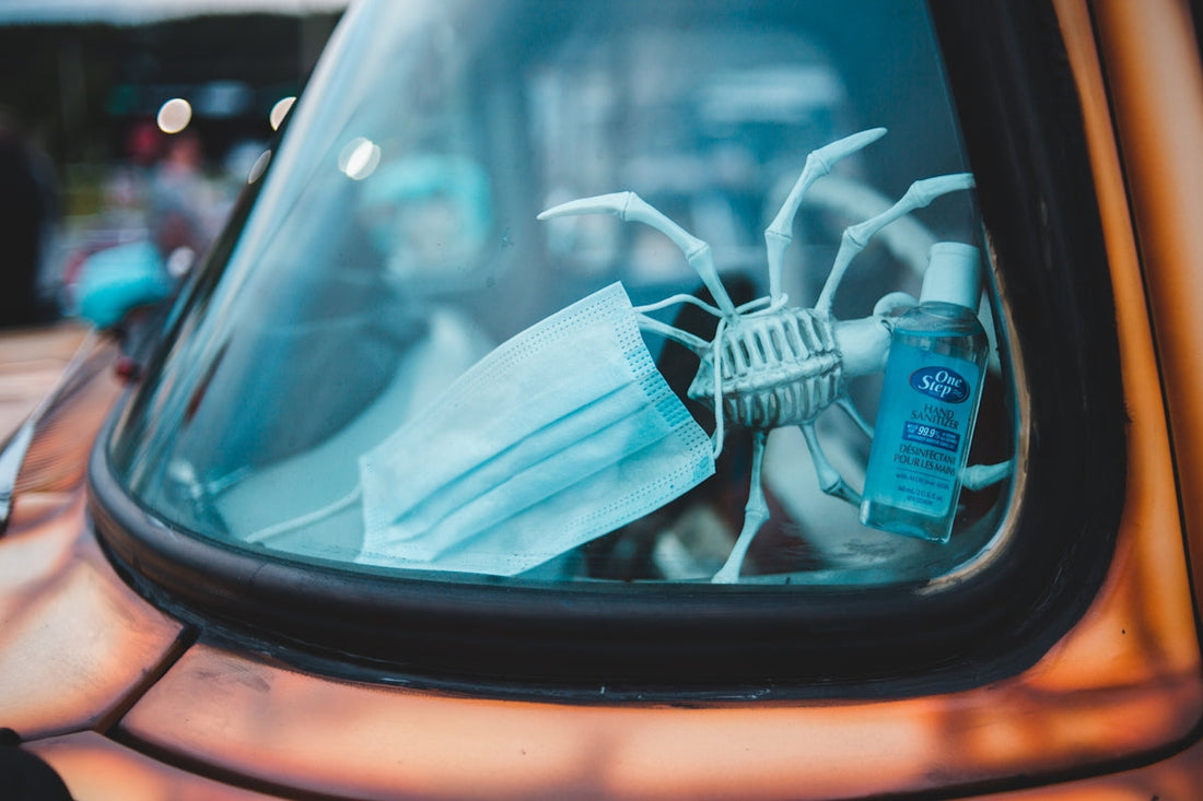 Close-up of a car dashboard featuring a facehugger model holding a face mask and hand sanitizer
