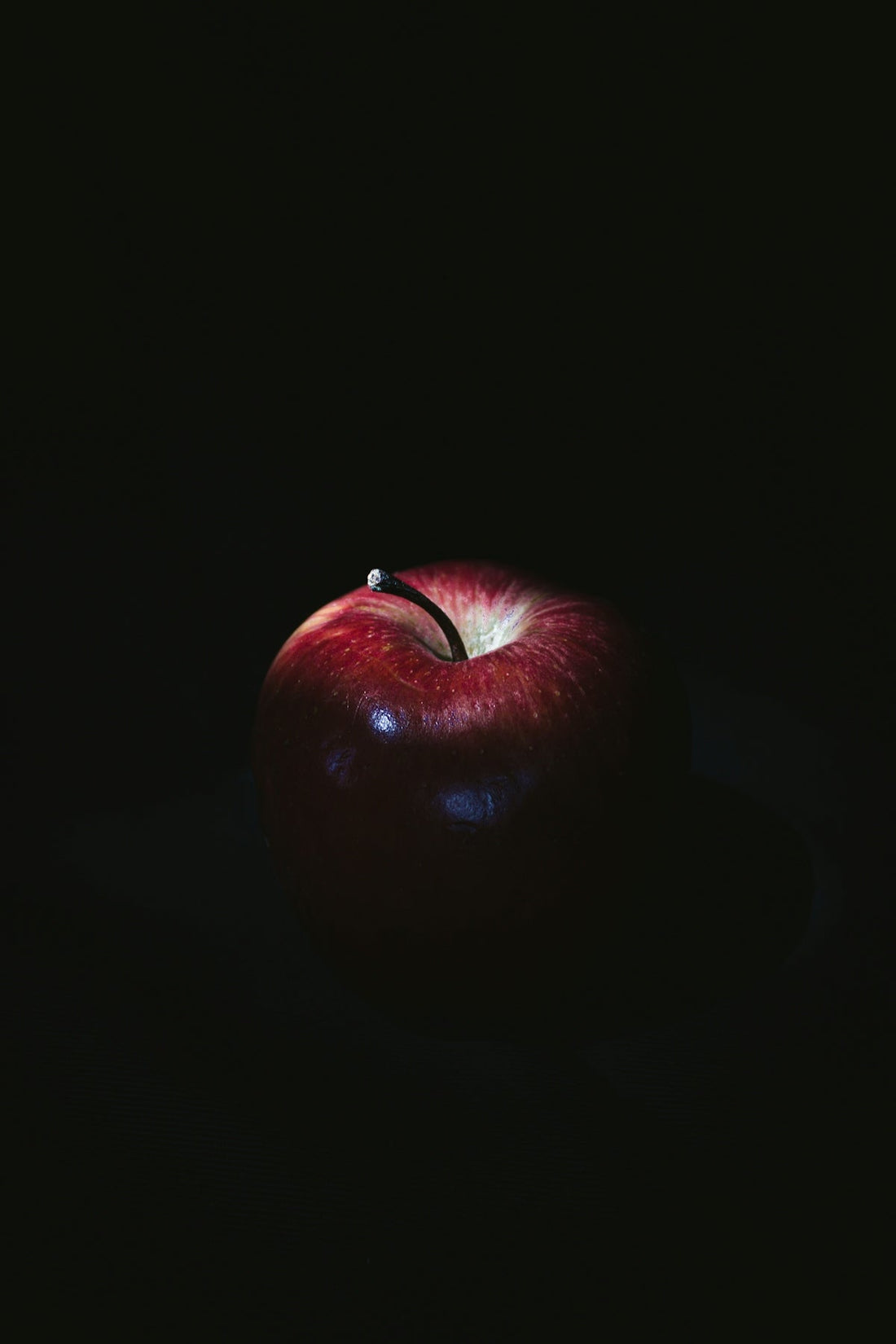 Red apple with stem on dark background, illuminated by dramatic lighting