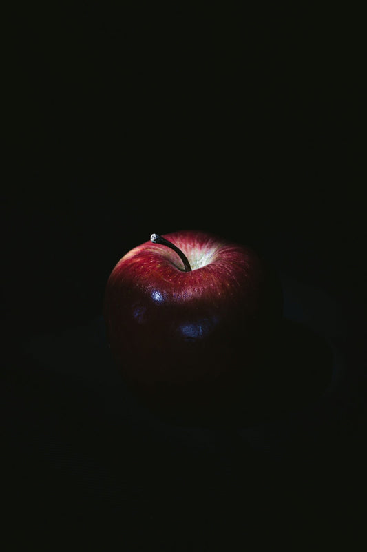 Red apple with stem on dark background, illuminated by dramatic lighting