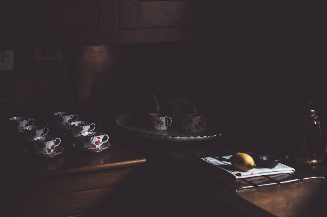 Vintage tea set and lemon on dark wooden kitchen counter, soft moody lighting