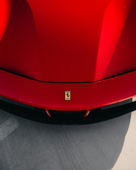 Front hood of a red Ferrari sports car with Ferrari logo, parked on concrete