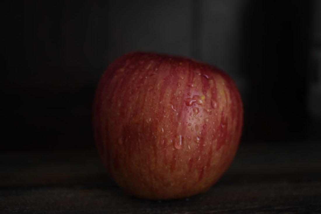 Close-up of a fresh red apple with water droplets on a dark rustic surface