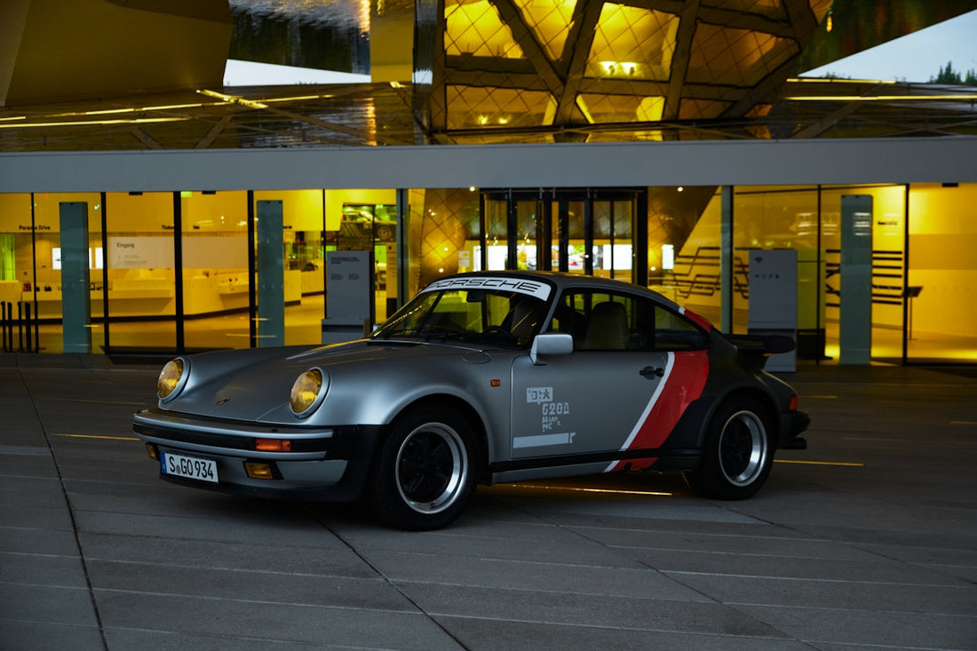 Classic silver Porsche 911 with custom red and black graphics parked in front of modern glass building