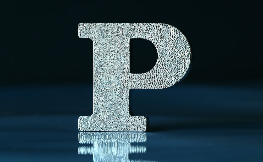 Metallic textured letter P standing on reflective surface with dark background