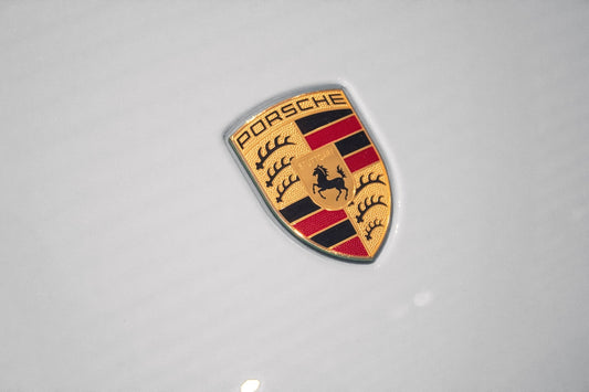 Close-up of Porsche car emblem on a white hood, luxury sports car logo detail