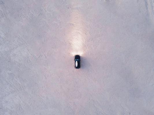 Aerial view of a black supercar driving on a sandy surface with headlights on