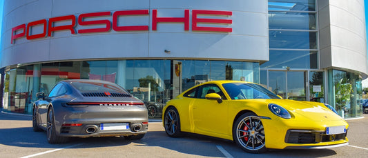 Yellow and gray Porsche sports cars parked outside modern Porsche dealership