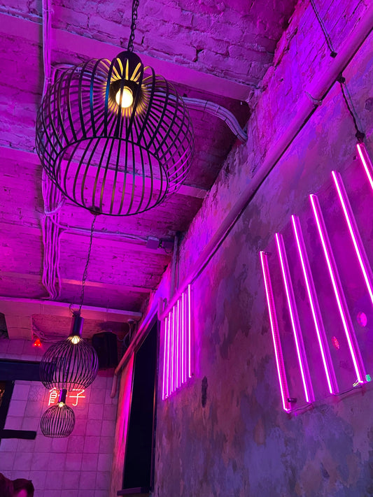 Industrial ceiling with modern pendant lights and pink neon wall lights in a nightclub setting
