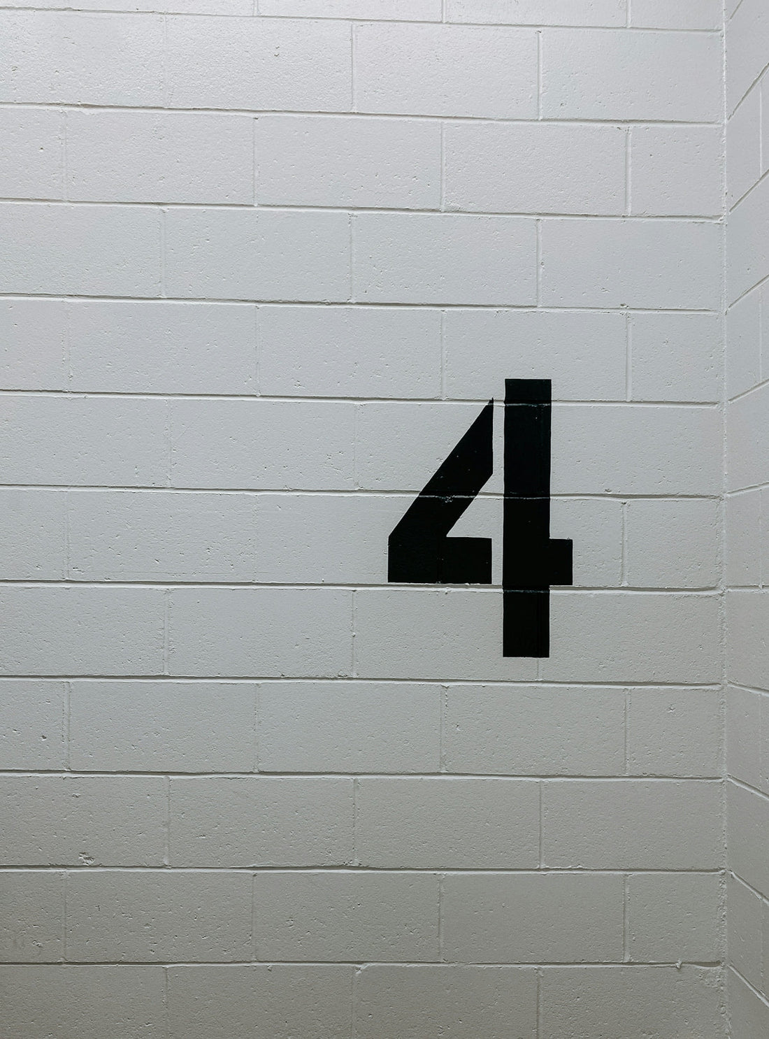 Large black number 4 painted on white cinder block wall, industrial staircase setting