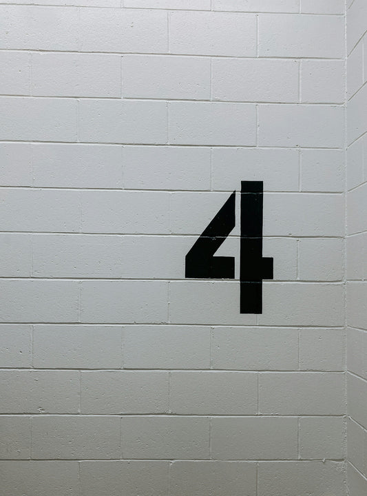 Black number 4 painted on a white cinder block wall in a stairwell or parking garage