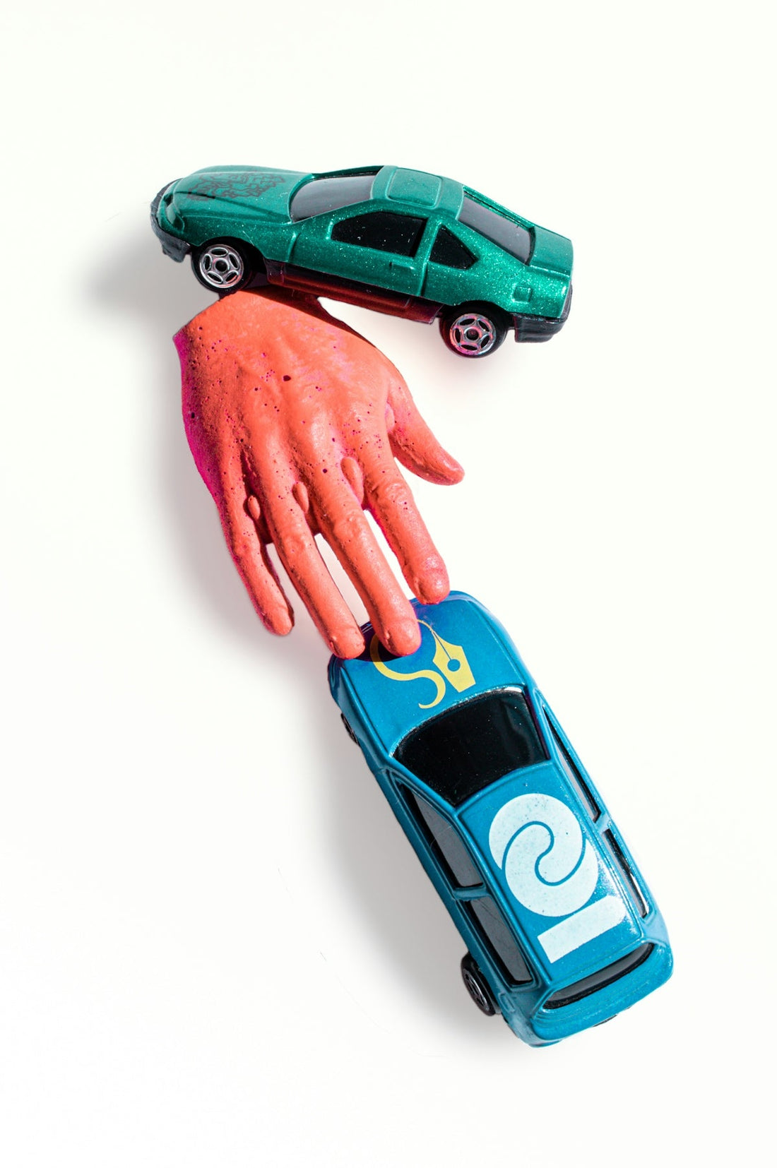Two toy car models and a painted hand sculpture displayed on white background