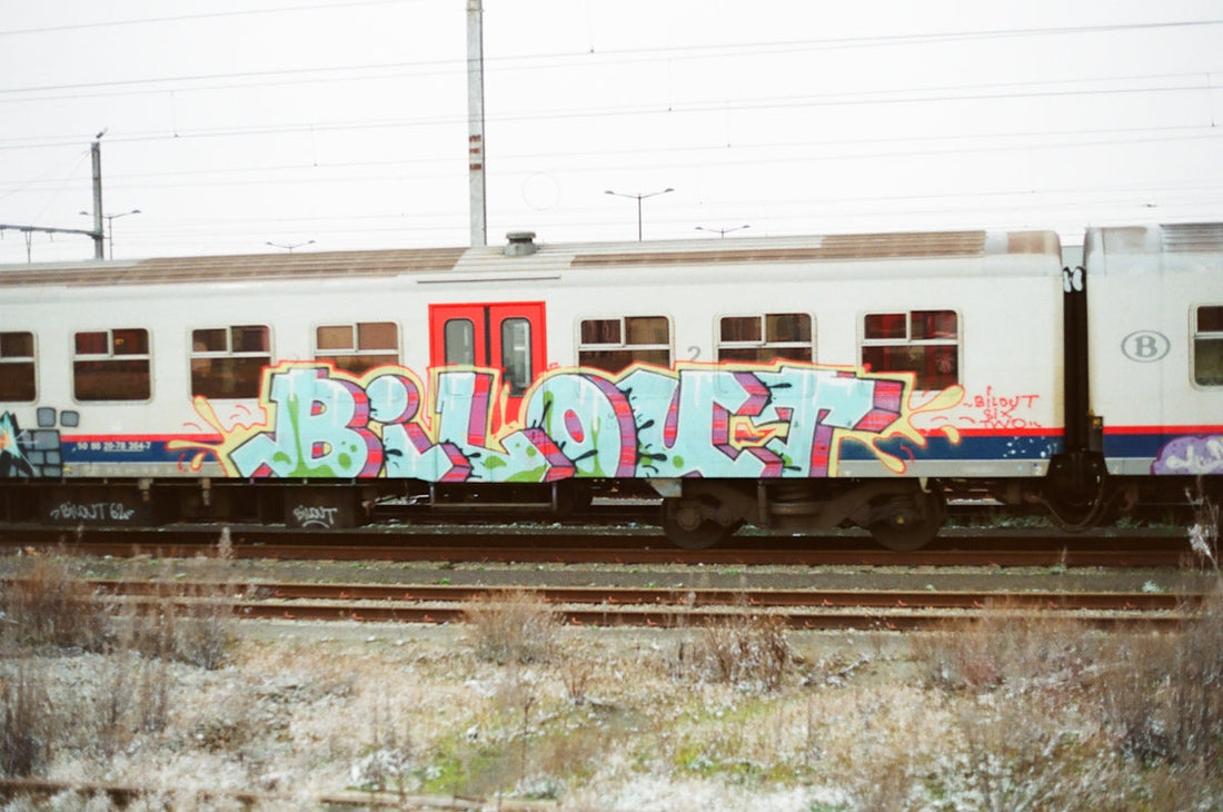 Train car with colorful graffiti art and bold lettering parked on railway tracks