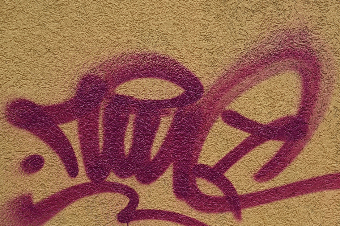 Close-up of purple graffiti tag on textured beige wall, urban street art style.