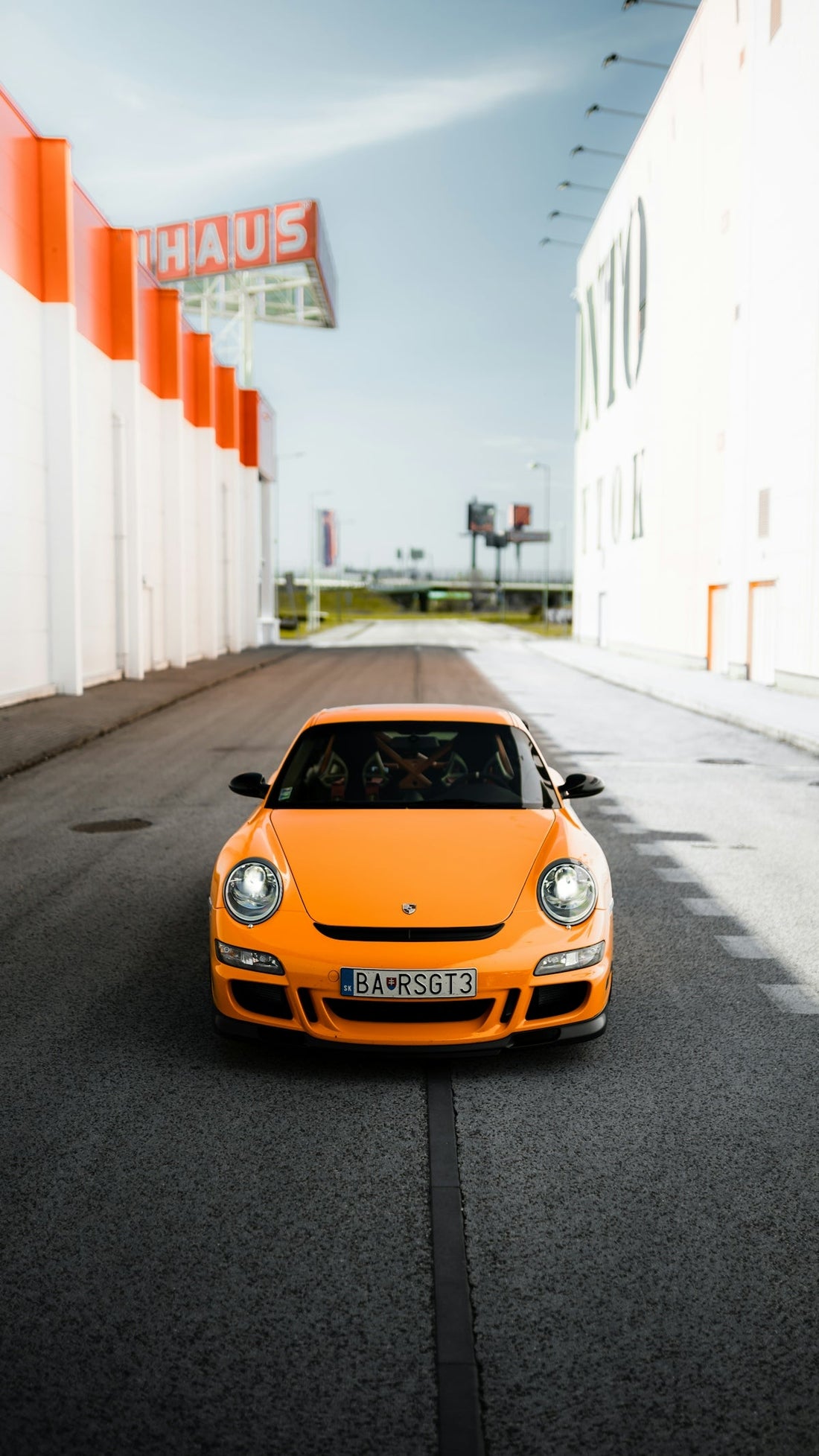 Bright orange Porsche sports car parked on urban street between modern buildings