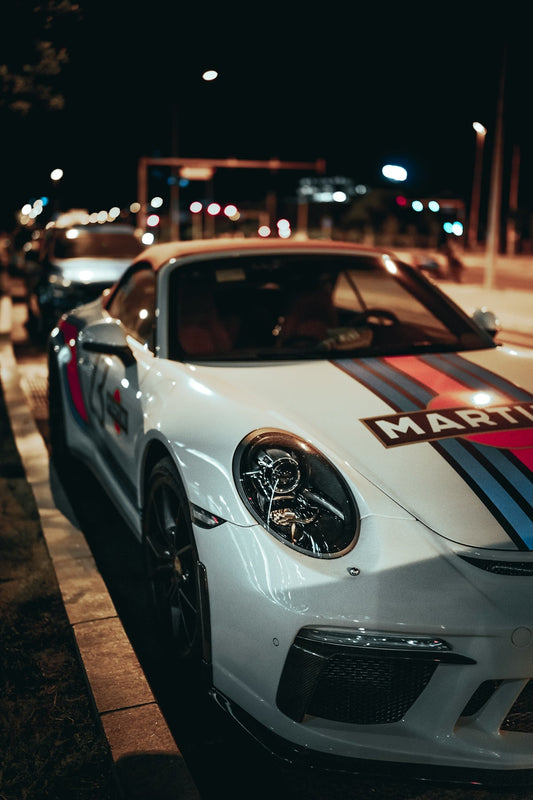 White luxury sports car with racing stripes and custom decals parked on city street at night