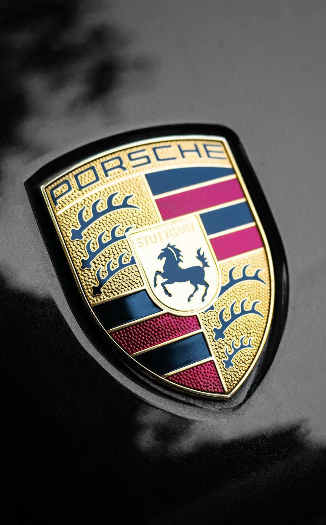 Close-up of a Porsche emblem on a black luxury car hood