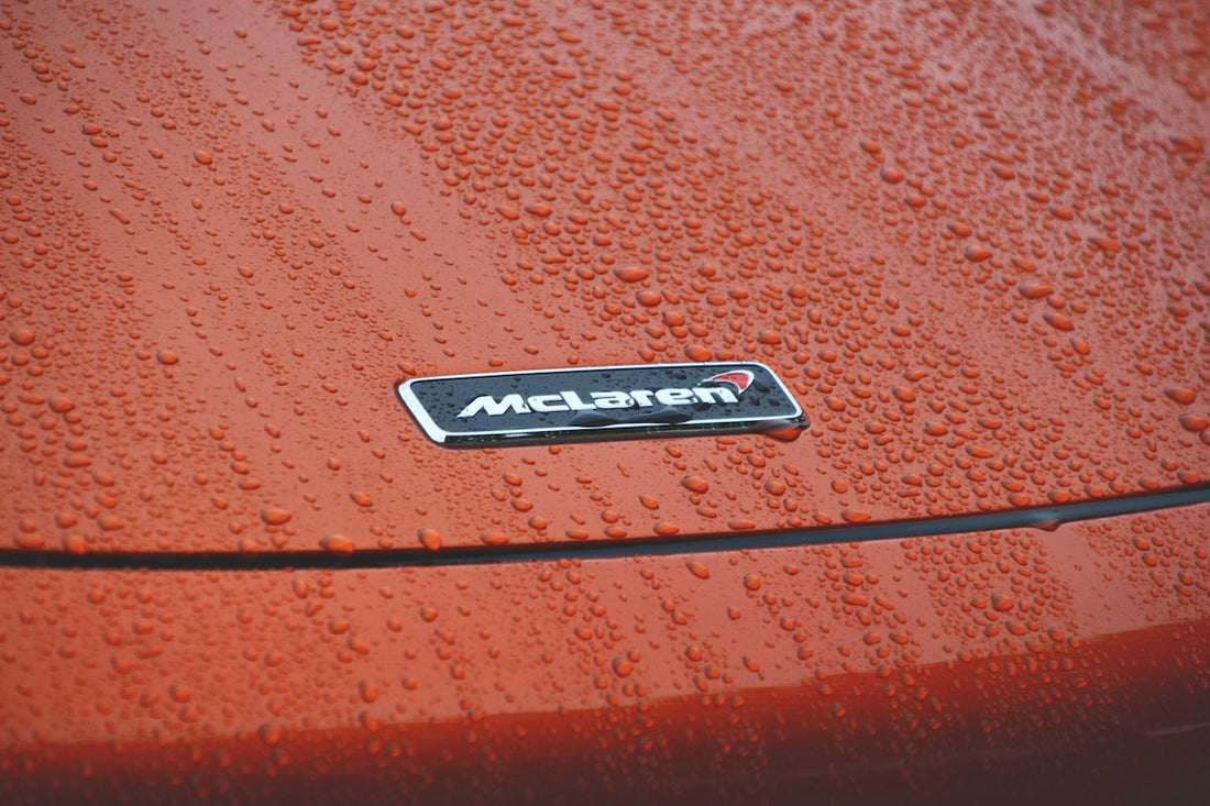 Close-up of McLaren badge on orange supercar hood with rain droplets