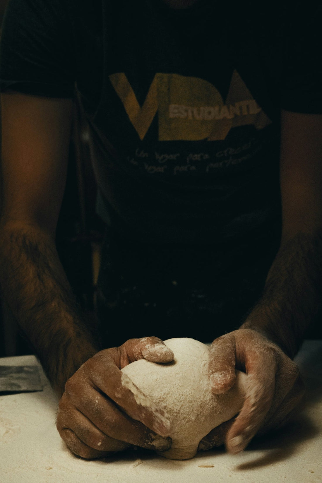 Person kneading dough on a floured surface, close-up of hands in dim lighting