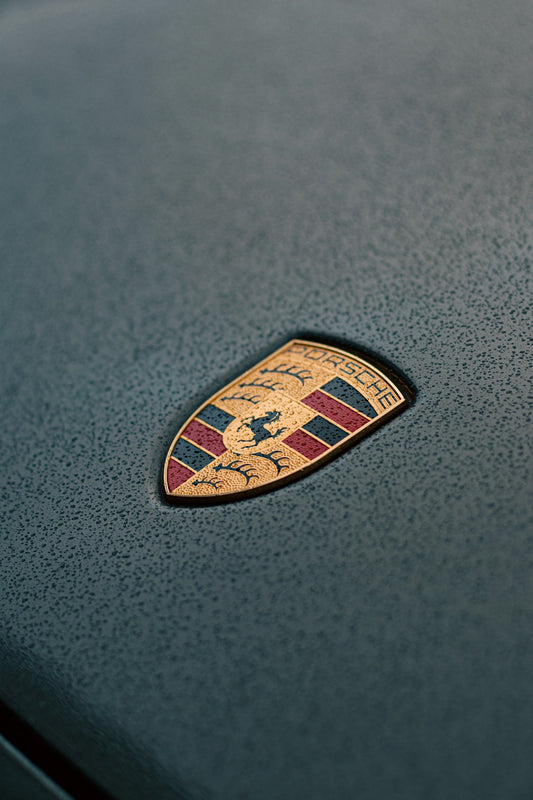 Porsche hood emblem with rain droplets on grey luxury car surface