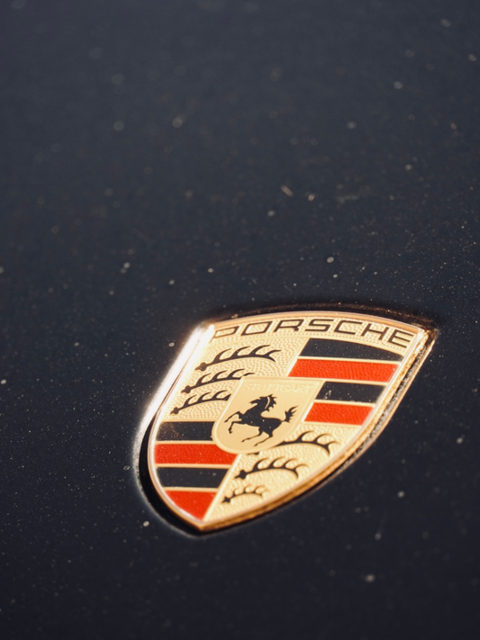Close-up of Porsche emblem on a dark car hood, luxury sports car badge