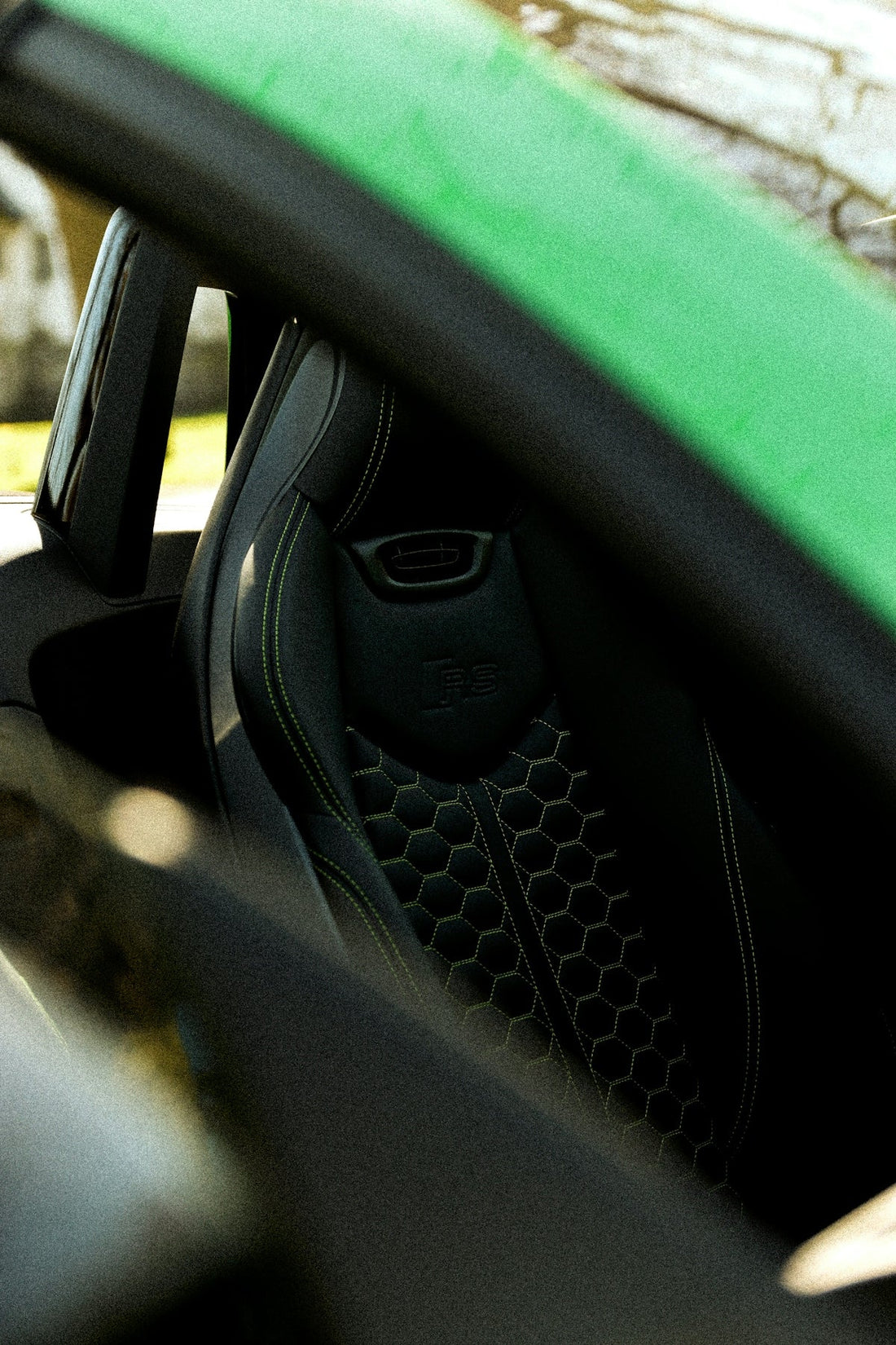 Luxury sports car interior with black leather RS seat and green stitching, seen through window