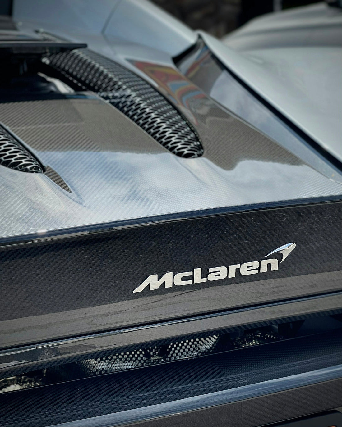 Close-up of McLaren car carbon fiber engine cover and logo, luxury exotic sports car