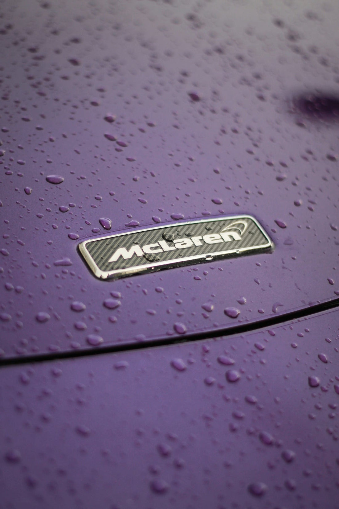 McLaren badge on purple car hood with water droplets, supercar exterior detail
