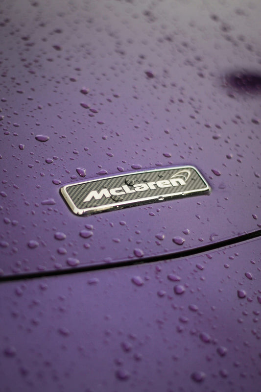 McLaren badge on purple car hood with water droplets, supercar exterior detail